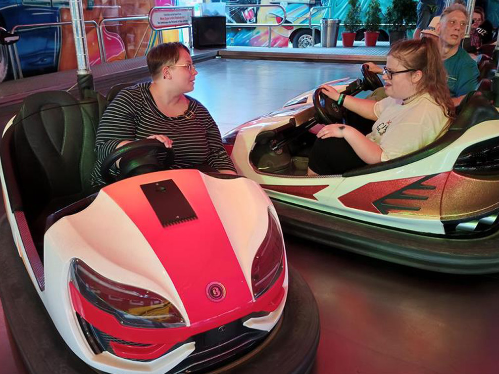 Zwei Frauen sitzen jeweils in einem Auto beim Autoscooter und unterhalten sich.